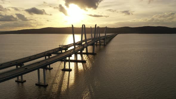 An aerial shot along the north side of the Mario M. Cuomo Bridge during a golden sunset. The drone c