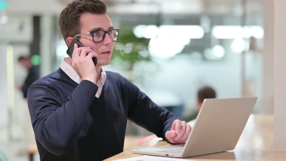 Young Businessman with Laptop Talking on Smartphone 