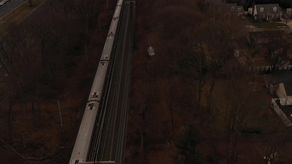 An aerial view over railroad tracks on a cloudy day. As a train approaches, the camera dolly out ove