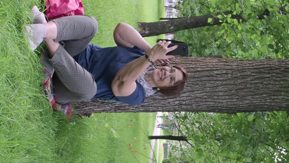 Senior Woman Having Video Call While Sitting on the Grass in City Park.