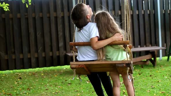 boy and girl ride on a swing in the village. older brother hugging little sister. slow motion