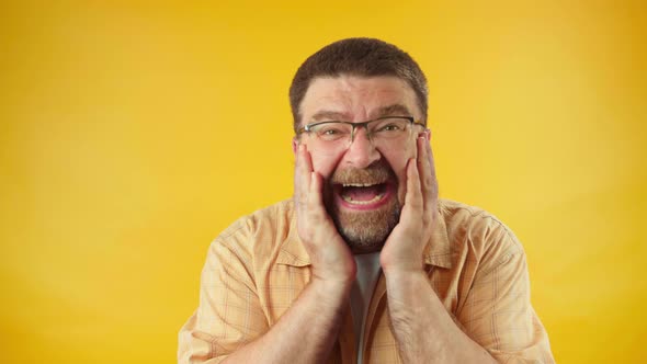 Bearded man in yellow shirt sincerely laughing against orange background, happiness,
