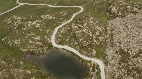 Cinematic Aerial View Gravel Trail Road Near Small Lake on the Mountain. Cloudy Weater, Mist and