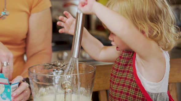 Adorable little girl toddler helps grandma in the kitchen by mixing the cream, pudding or sauce