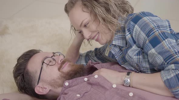 Close Up Portrait of Man and Woman Lying Together on Fluffy Carpet and Talking. Bearded Man in