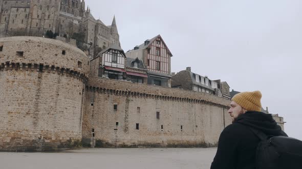 Camera Moves Around Happy Excited Tourist Man with Backpack Stunned By Epic Mont Saint Michel Castle