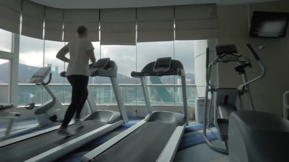 Woman exercising on running machine in front of panoramic window