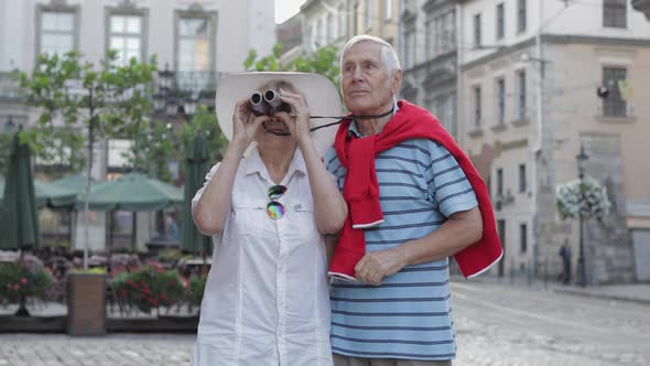 Senior Male and Female Tourists Walking in Town Center and Looking in Binoculars