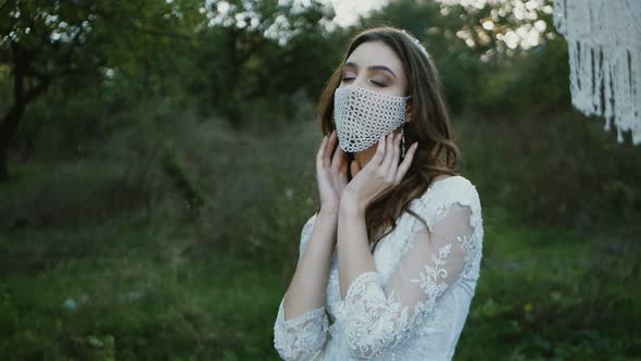 portrait of a bride in a mask posing. Beautiful young bride in a wedding dress in the park. On her f