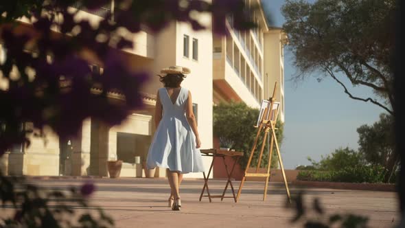 Slim Beautiful Creative Caucasian Woman in Elegant Dress and Straw Hat Walking to Canvas on Easel in