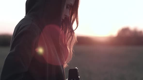 Female Stands in Field with Vintage Camera on Background Sunset with Sun Glare