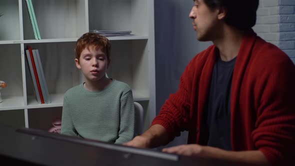 Side View of Schoolkid Boy Sings Song with Music Teacher Playing Piano at Home During Lesson