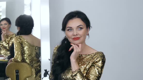 A Beautiful Showy Young Woman with a Stunning Evening Make Up Smoky Eyes in a Sparkling Gold Dress