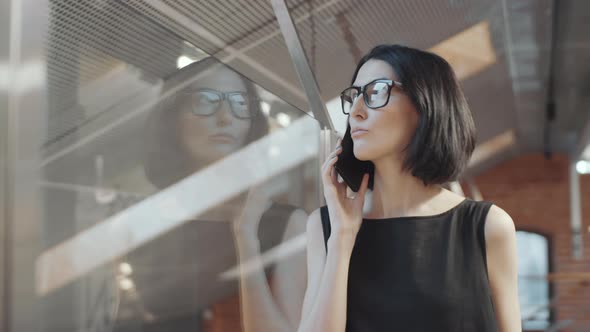 Business Lady Chatting on Mobile Phone beside Glass Wall in Office