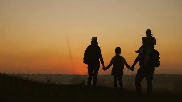 Silhouettes of Father, Mother and Children Hiking. Baby Sits on the Shoulders of His Father. Hiking