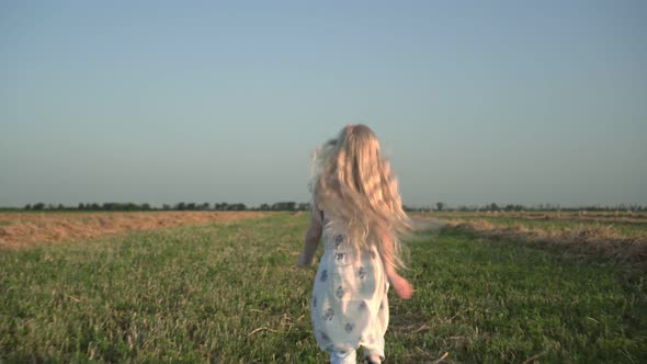 A Child Girl with Long White Hair Runs Across a Rural Field