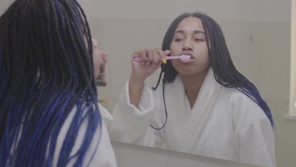 Reflection in Mirror of African American Woman Brushing Teeth. Teenager Getting Ready in the Morning