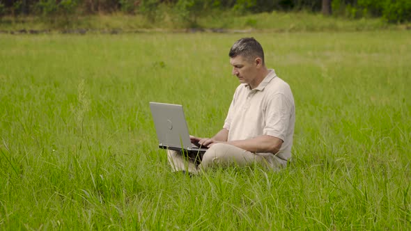 Freelancer Uses Laptop for Remote Work Sitting on the Lawn in the Grass