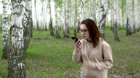 A Young Woman Is Looking for a Cellular Network in a Birch Forest. A Girl Is Talking on the Phone