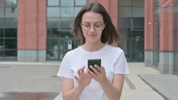 Young Woman Browsing Internet on Smartphone while Walking on Street