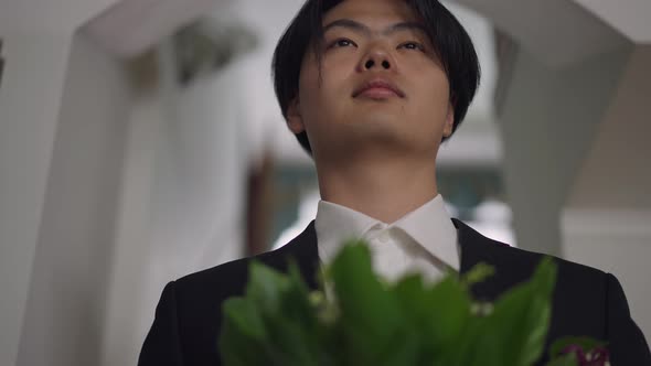 Closeup Portrait of Happy Young Asian Groom Standing with Bouquet Indoors Looking Away