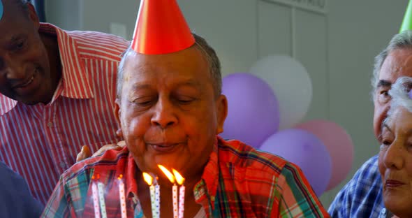 Senior man blowing out the candles on a birthday cake with his friends 4k