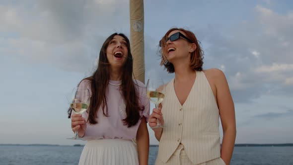 Two Girlfriends in a Good Mood Drink Wine While Walking on a Yacht