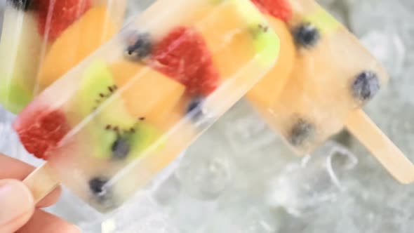 Homemade fresh fruit popsicles with apple juice on metal tray with ice cubes.