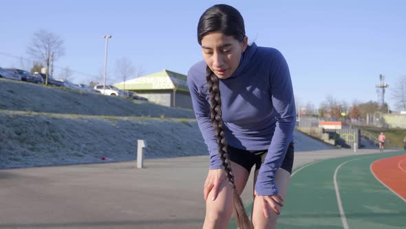 Athletic Hispanic Woman Stops Jogging to Take Breather with Hands on Knees