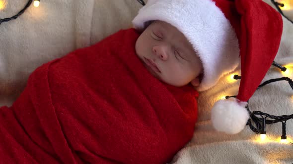 Close Up Portrait First Days Of Life Newborn Cute Funny Sleeping Baby In Santa Hat Wrapped In Red