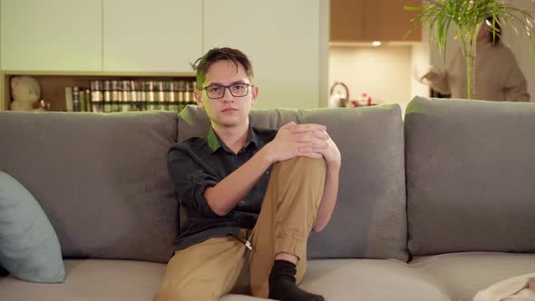 A Guy with Glasses Watches TV on the Sofa in the Evening in the Living Room