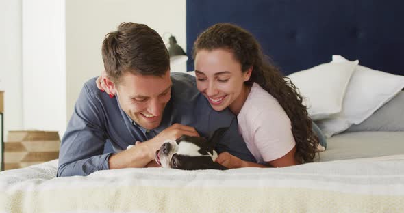 Caucasian couple playing with dog in bad at home