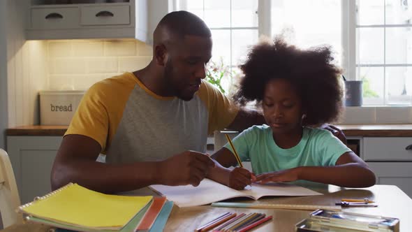 African american daughter and her father doing her schoolwork together at kitchen table