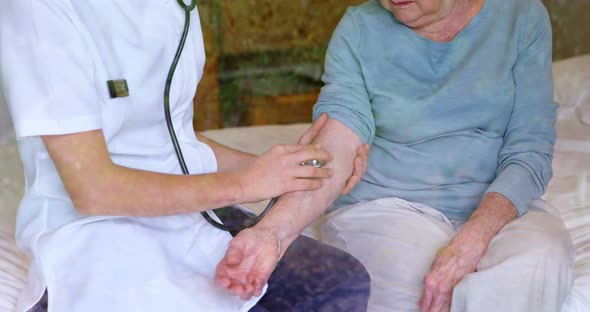 Doctor Checking Senior Woman Pulse Using Stethoscope on Bed