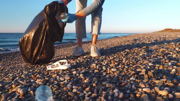 a female volunteer collects garbage in a black garbage bag.