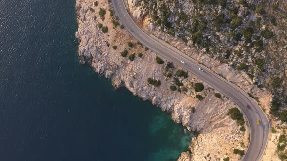 Birds Eye View of Asphalt Mountain Road with Driving Cars Above the Blue Sea