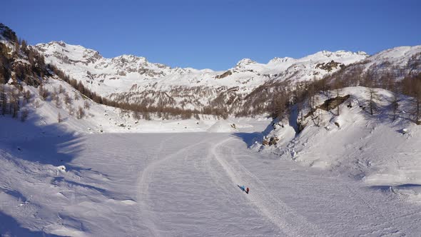 Aerial View of People Walking Across a Snow Covered Area in the Sun . Mountain Shadow Covering Part