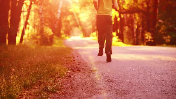 Sport Man Running at Asphalt Road. Rural City Park. Green Tree Forest and Sun Rays on Horizon.