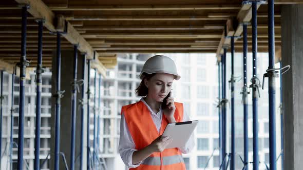 Young female civil engineer in safety jacket and helmet is talking on mobile phone