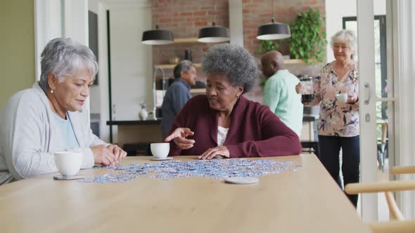 Group of happy diverse senior friends drinking coffee and doing puzzle at home