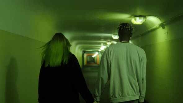 Refugee couple walking inside the corridor of a concrete bunker serving as a bomb shelter, back view