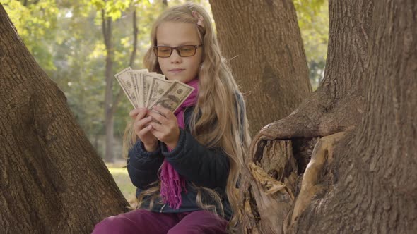 Young Blond Caucasian Girl in Photochromic Glasses Counting Money and Thinking As Sitting