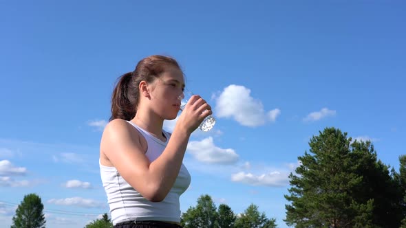 Athletic Young Woman Drinking Water From a Glass in the Park on a Sunny Day