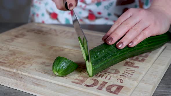 A woman in a kitchen cutting up a cucumber in to slices on a wooden chopping board