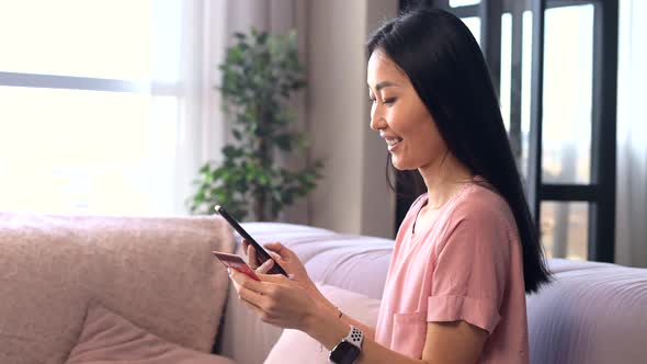 An Attractive Young Asian Woman is Using a Smartphone for Shopping Online