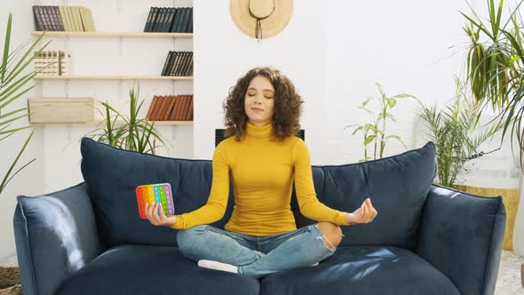 Young Woman Meditating with Trendy Pop Toy in Lotus Pose at Home
