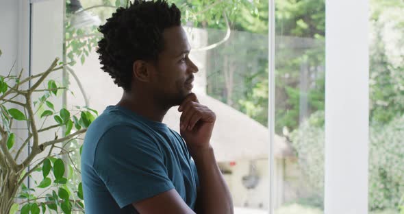 Thoughtful biracial man standing at window and looking into distance