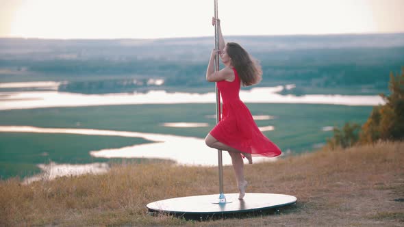 Young Woman in Pink Dress Climbs on the Pole