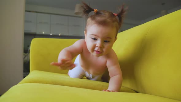 Cute Little Baby Girl on the Yellow Sofa Making First Steps At Home