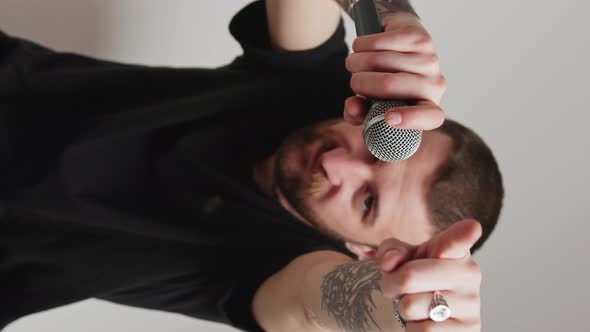 Vertical Video Attractive Caucasian Man Moves Hands Microphone in Hands Pointing to the Camera Grey